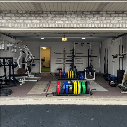 Fleming Athletics garage gym — squat rack, bumper plates, and dumbbells